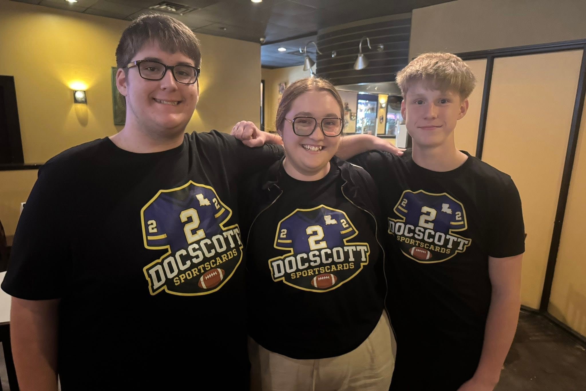 Three people wearing matching black t-shirts with a logo and text in an indoor setting.